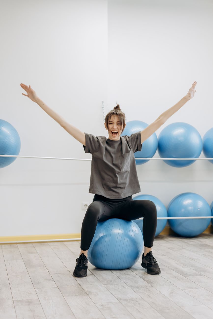 Imagen ilustrativa: mujer sentada en una pelota de ejercicio con los brazos arriba